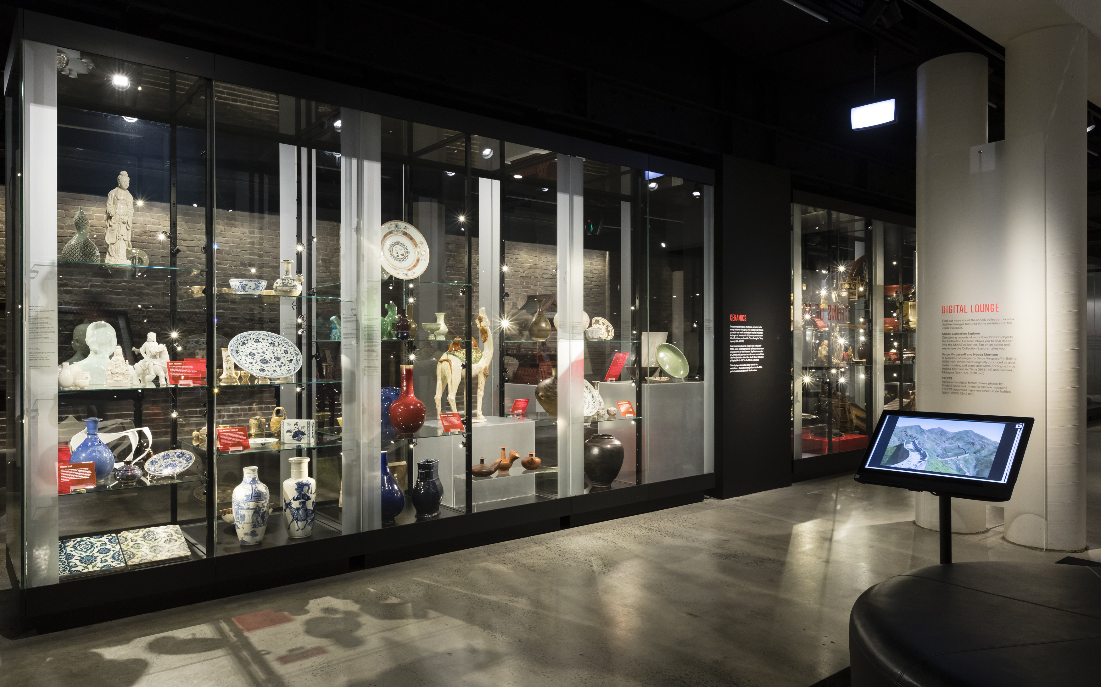 View of tall glass showcases with about 50 large and small ceramic pieces on shelves. On the left, digital lounge with a computer screen is shown.
